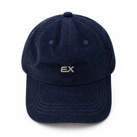 A dark navy blue corduroy baseball cap with a small silver 'EX' logo on the front, displayed on a light beige fabric background.