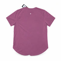 A mauve pink short-sleeve athletic top shown from the back, laid flat on a tan surface. A small circular logo is centered near the neckline, and a hangtag is visible at the top.