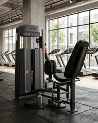 An hip adductor machine in a modern gym setting with treadmills and large windows in the background.