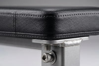 Close-up detail of a black textured padded surface, likely a bench or stool cushion, attached to a silver metal support frame with a visible threaded bolt and washer.