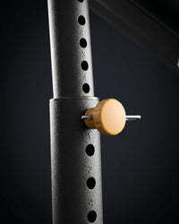 Close-up of a black adjustable weight bench leg with numbered height slots and a round tan adjustment knob with a metal pin.