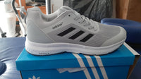 A pair of Adidas running shoes in gray, placed on a box with blue and white Adidas branding.